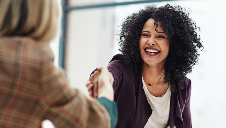 Smiling professional woman shaking hands with a new hire in a modern office setting.